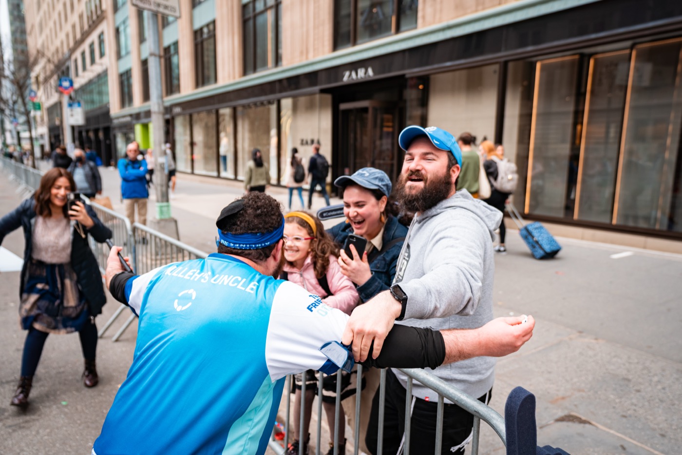 Team Friendship runner hugging family through a barrier during a race — multi-generational, warm, unposed joy.