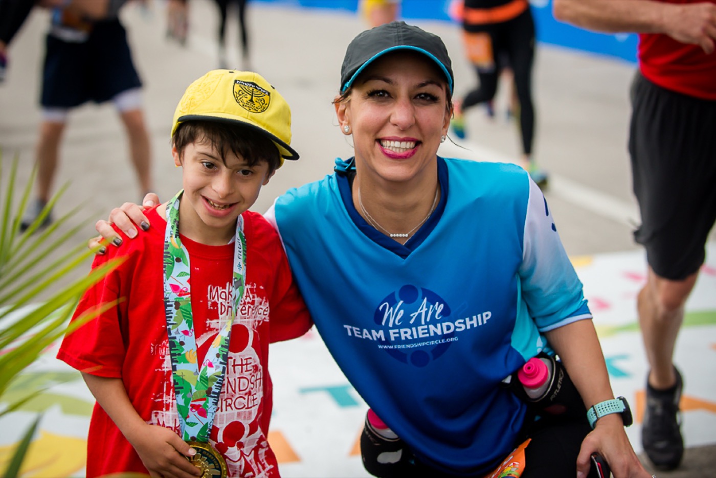 Team Friendship runner alongside a child buddy wearing a medal at a finish line — beaming together, warm, arm around shoulder.